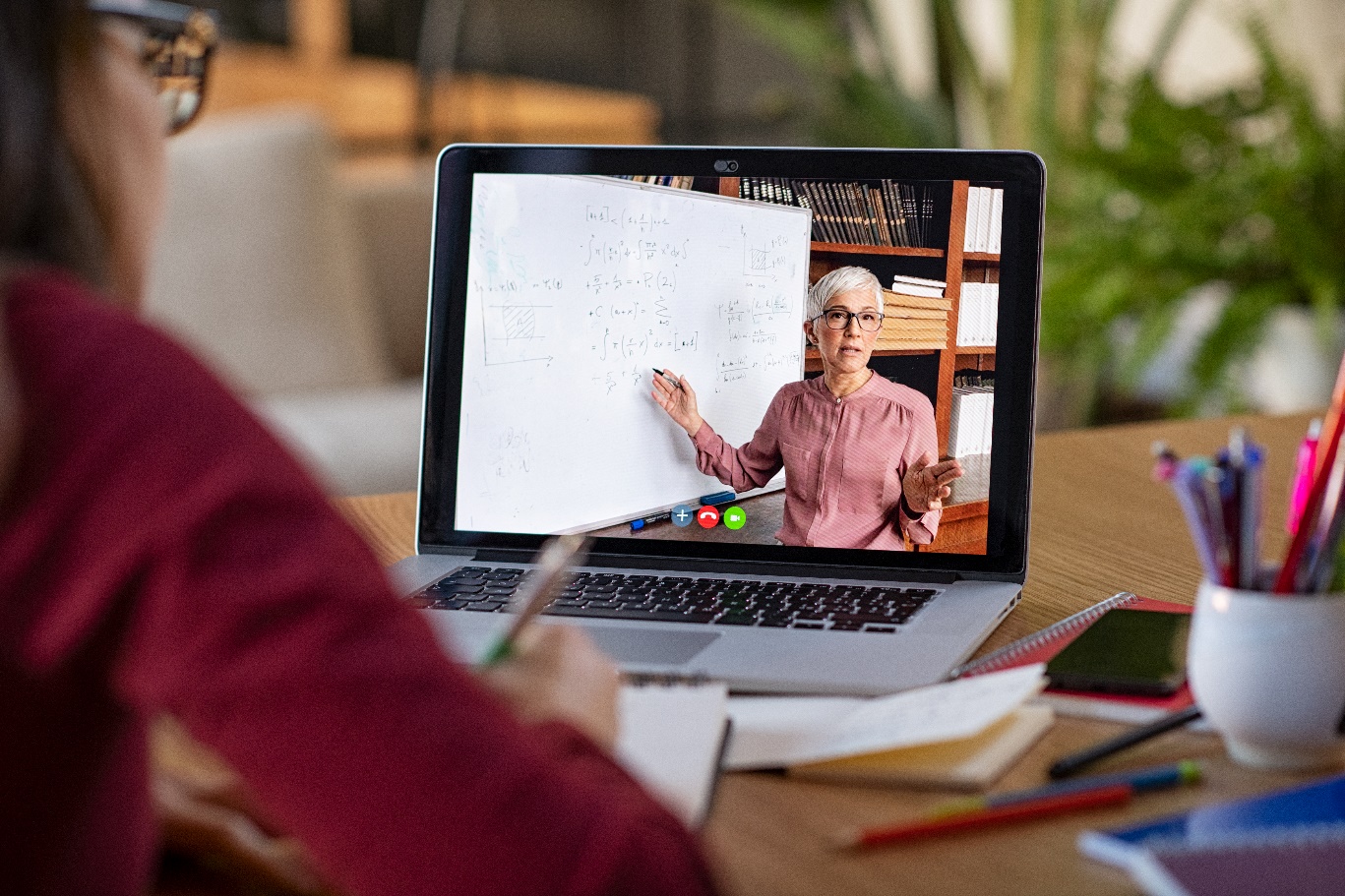 student attending an online class on laptop taking notes